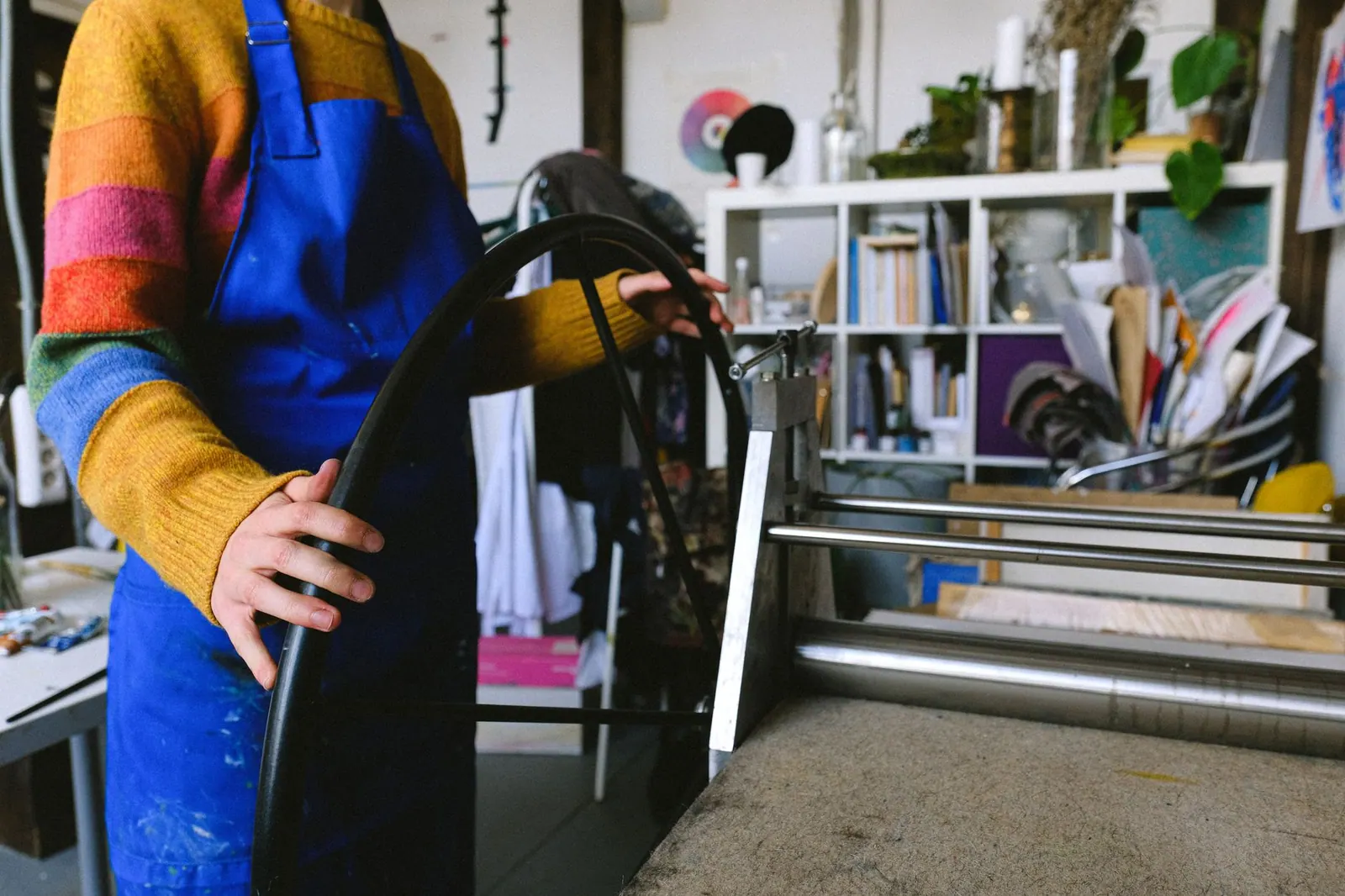 Side view of unrecognizable female painter in blue apron turning wheel of etching printing press machine in craft shop. Gelatin Plate Monoprint Recipe: A Reusable Printmaking Surface