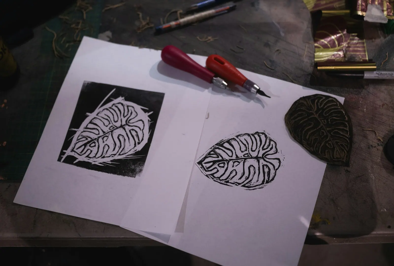 A linocut print of a leaf beside a carving tool on paper. Linocut Reduction Prints, Step by Step: Many Colors from a Single Block