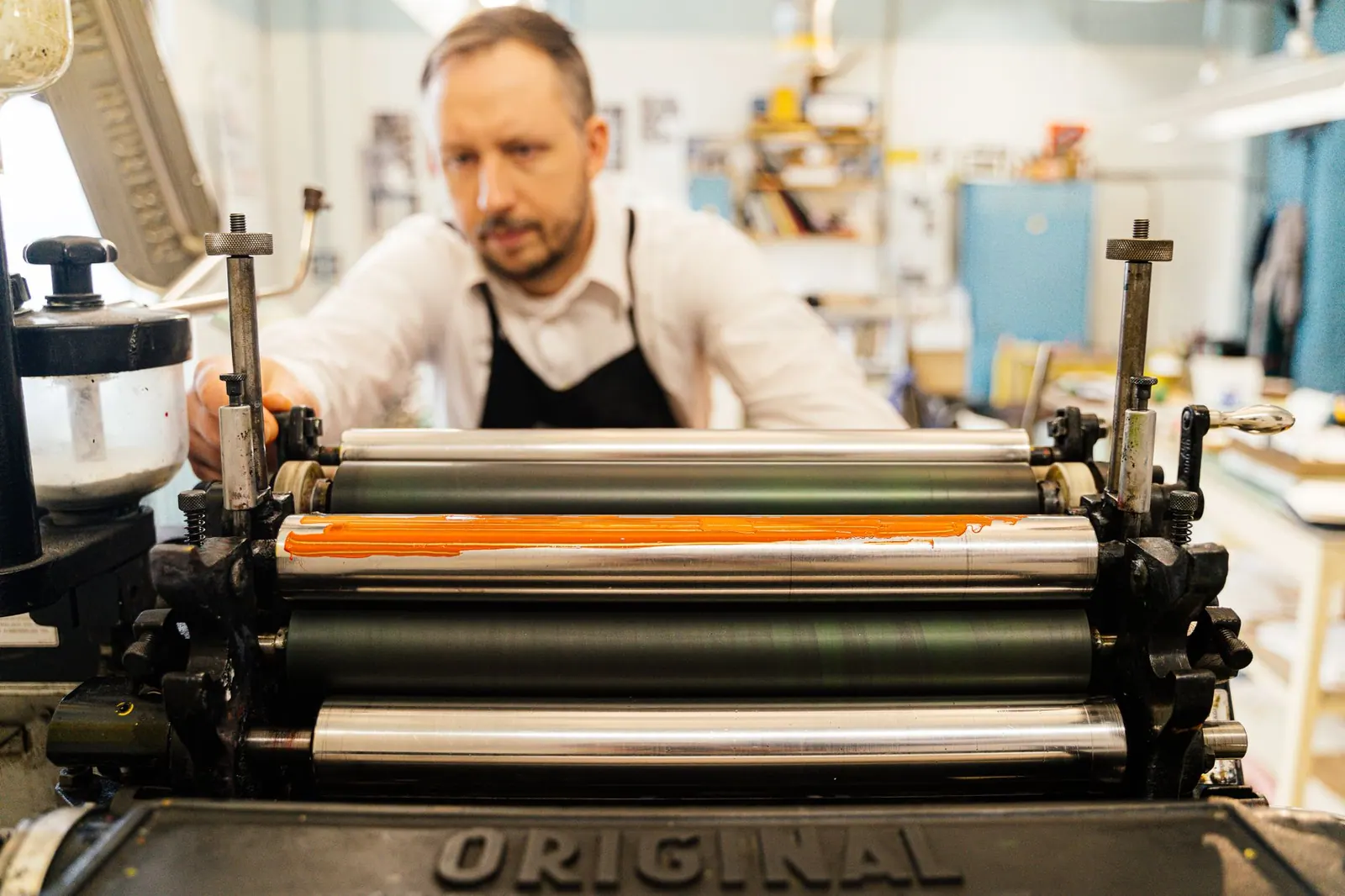A focused man operates a vintage printing press in a well-lit workshop, highlighting traditional craftsmanship. How to Wash Cyanotype on Fabric Without Fading the Blue